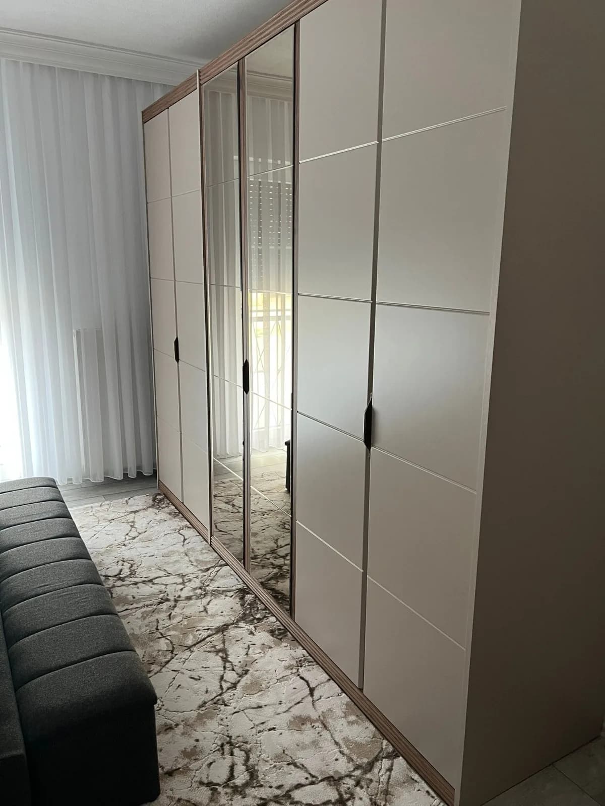 Grande armoire de chambre aux portes blanc cassé rainurées, dont deux portes miroir au centre