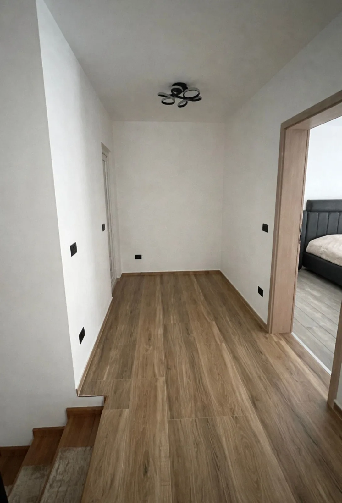 Palier lumineux aux murs blancs, sol en lames d'aspect bois avec plinthes assorties, haut d'escalier à gauche et porte ouverte sur une chambre
